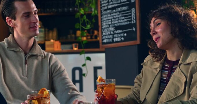 Slow Motion Of Friends Toasting Cocktails During Social Gathering In Modern Caf&eacute;. Young adults raising colorful cocktails for a cheerful toast inside a contemporary caf&eacute; or lounge.
