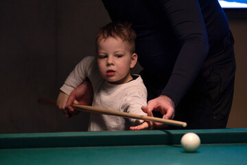 Fototapeta premium Parent teaching young child to play billiards on pool table indoors