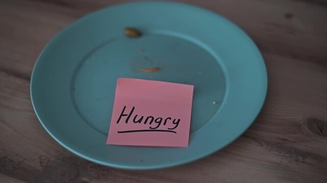 A plate is shown that is mostly empty, with a note placed on it that reads Hungry. This setup suggests a moment of longing for food, capturing a relatable feeling