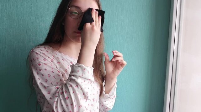 Teen girl wiping eyeglasses lens close up, vision care routine, personal maintenance and lifestyle concept.