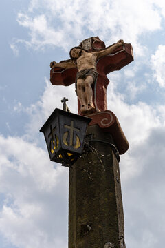 View of a historic stone crucifix with a sculpted figure of Jesus and an attached lantern against a cloudy sky in Monreal, Rhineland-Palatinate, Germany.