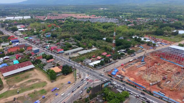 Cinematic tracking shot rotating over a large building foundation Features heavy machinery urban roads and local housing toward green hills in a wide and evolving eastern district