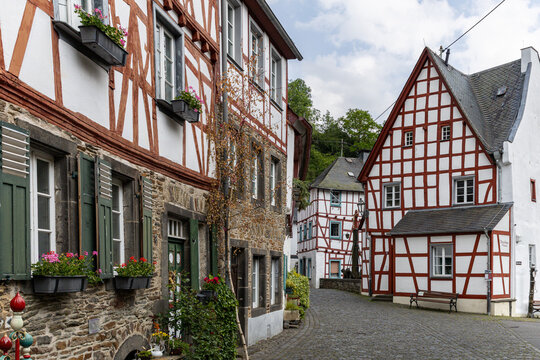 View of traditional half-timbered houses with red frames and flower boxes along a narrow cobblestone street in the historic village of Monreal, Rhineland-Palatinate, Germany.