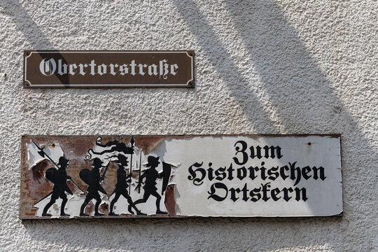 View of street signs on a textured wall, including a sign for Obertorstrasse and a directional sign with medieval soldier illustrations Monreal, Rhineland-Palatinate, Germany.