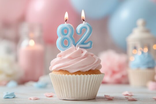 Festive celebration cupcake with pink frosting and candles shaped as the number eighty-two
