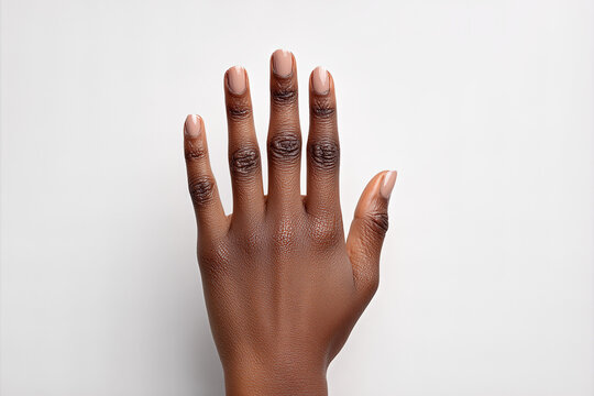 Black female hand model with glossy nude manicure, fingers extended upward against white background, textured skin and almond nails in studio lighting