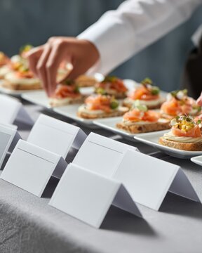 Event staff arranging blank place cards beside plated appetizers on catering table