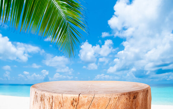 Aged wooden stump pedestal for product display on blurred tropical sea sand beach, sky and green palm leaf background