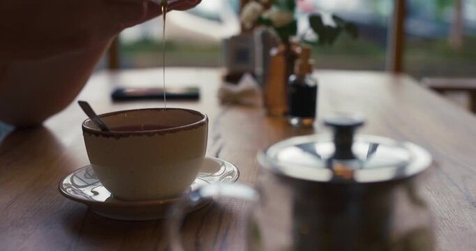 Relaxed morning scene with person add a spoon of honey and drinking tea in a cozy cafe