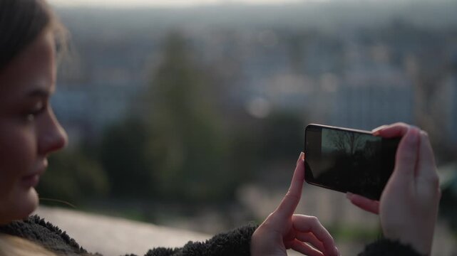 A woman in Paris France is taking a photo with her smartphone of the city skyline at sunset The handheld shot captures the travel love and technology concept.