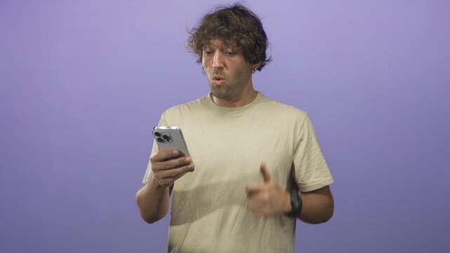 Hispanic man holding smartphone, thumb visible while scrolling and reacting with a thumbs up gesture in a studio; surprise approval.