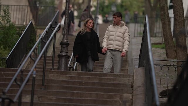 A couple walks down a set of stairs in Montmartre Paris France The handheld shot captures the romantic walk as they descend the steps holding hands The scene is set in the urban environment of the cit