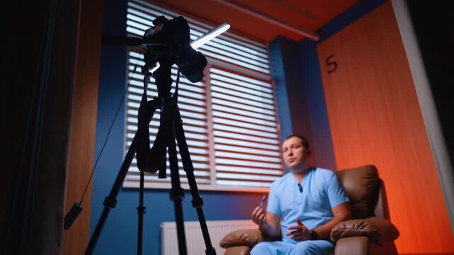 Professional camera and soffit are arranged in front of the man in armchair. Low angle view. Medical blog creation.