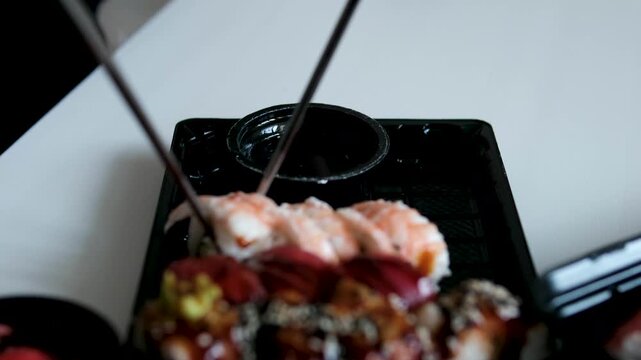 woman tries to eat sushi rolls with chopsticks but struggles to hold them correctly, using one stick in each hand. The playful scene captures a funny beginner moment after receiving a sushi delivery. 
