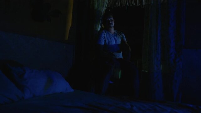Lonely transgender woman sitting on her bed at night, feeling worried, scared and paranoid