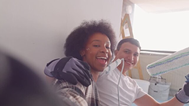 A young couple enjoys a light-hearted moment during their home renovation, surrounded by painting supplies and a ladder. The cheerful atmosphere contrasts with the work in progress.