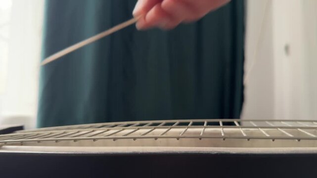 Person scraping wooden stick along metal radiator grille close up at home, producing rhythmic sound, improvised percussion activity, creative experiment
