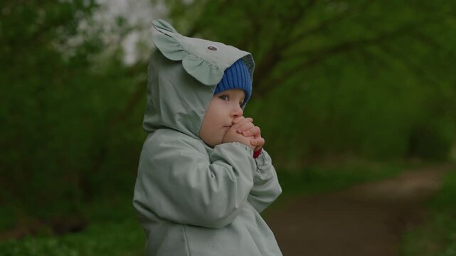 Slow motion handheld shot of a surprised toddler holding hands near face in the forest