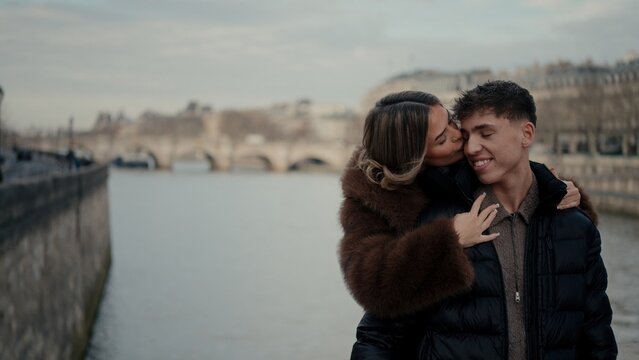A romantic couple embraces with the Paris cityscape in the background the woman kissing the man on the cheek. This image represents love and affection in France showcasing an urban lifestyle.
