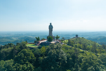 A large statue stands on top of a green mountain in the scenic landscape of Anlu Hubei in China © AS_SleepingPanda