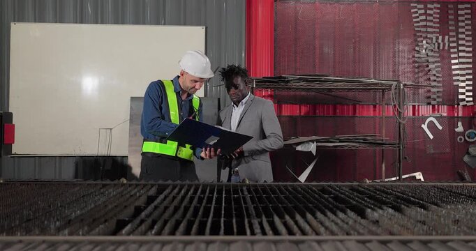 Sales engineer meets a client in an industrial workshop, reviewing quotation details, discussing costs and capabilities, and negotiating terms for a custom production project.
