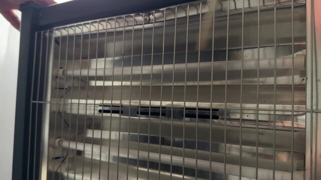 Person scraping wooden stick along metal radiator grille close up at home, producing rhythmic sound, improvised percussion activity, creative experiment