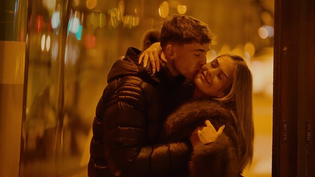 A young couple embraces and kisses in Paris France at night The warm lighting and urban city background create a romantic atmosphere perfect for Valentine's Day content.