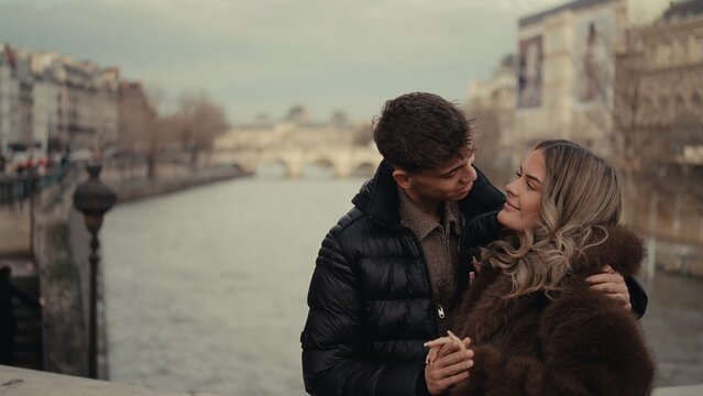 A romantic couple embraces in Paris France with the River Seine and cityscape in the background. This image conveys love affection and the urban lifestyle of travel and tourism.