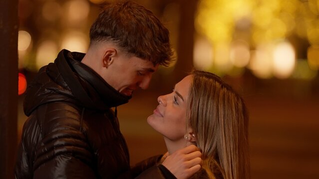A young couple in love embraces in Paris France at night with bokeh lights in the background. This image captures an affectionate moment of urban romance in a European city.