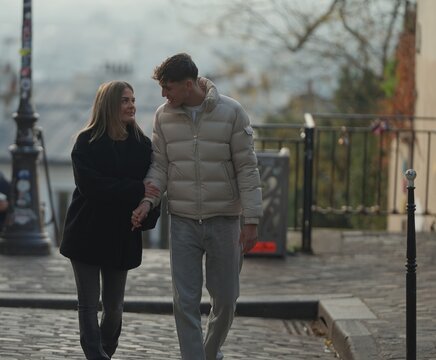 A romantic couple walks hand-in-hand on a cobblestone street in Montmartre Paris France They are wearing winter coats and jeans enjoying their love and travel experience in the city.