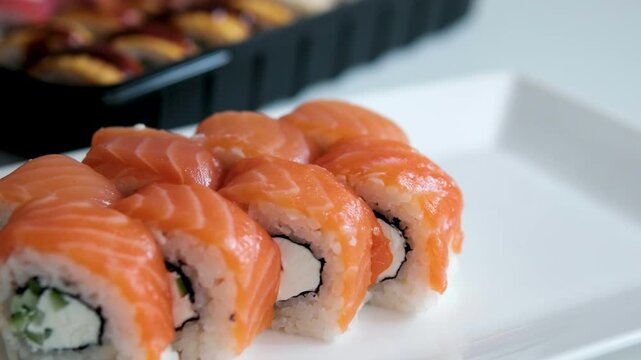 Female hands in transparent disposable gloves carefully transfer Philadelphia sushi rolls from black delivery box onto a white plate. scene captures neat food presentation, home dining aesthetics. 