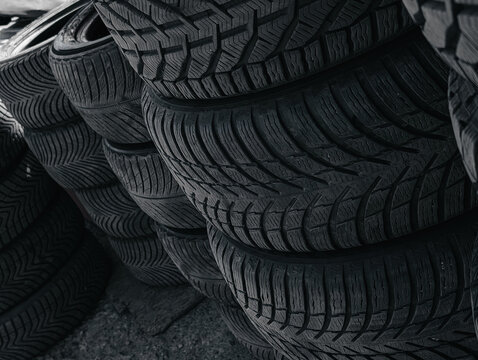 Close-up of stacked winter tires. Black car tires stacked diagonally, selective focus highlights the complex tread patterns and sipes designed for snow and ice conditions.