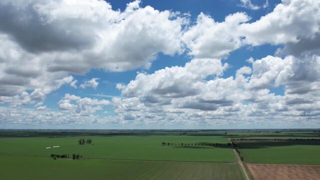High quality aerial timelapse showing cumulus and stratocumulus clouds changing shape and moving over vast green agricultural fields with fast shadows in the Santa Fe pampas region