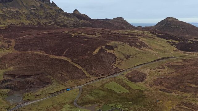Aerial view of a blue car driving along a winding road through the dramatic landscape of the quiraing on the isle of skye in scotland