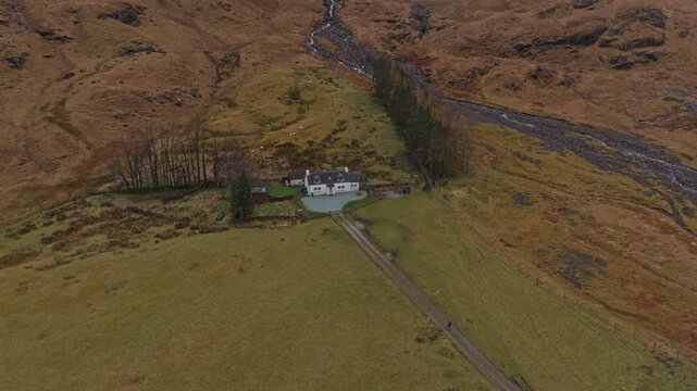 Aerial view circling a remote white cottage in the dramatic and rugged landscape of glen coe, scotland. A stunning natural scene