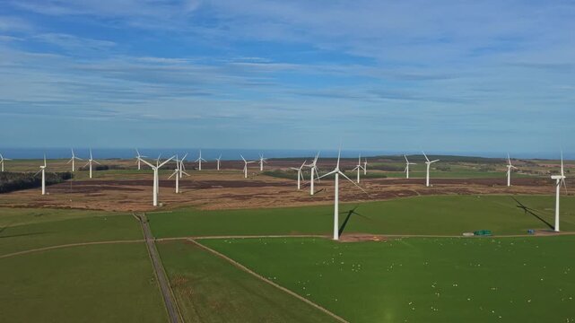 Drone footage capturing numerous wind turbines generating clean, sustainable electricity on a wind farm in the rural english countryside