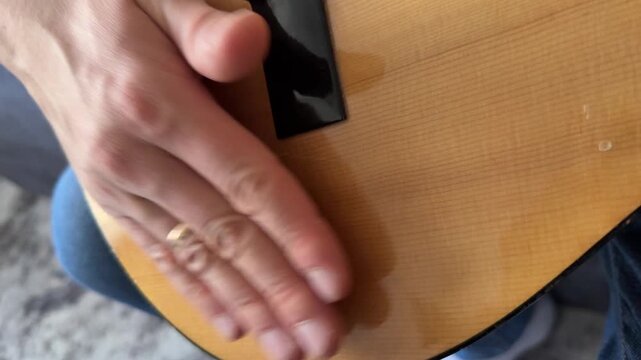 Person hitting acoustic guitar body with palm close up at home, producing strong rhythmic percussion sound, improvised music activity, creative hobby concept