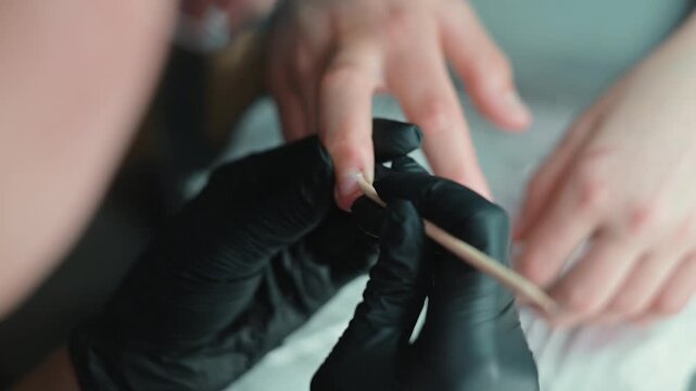 A person with light skin and applies nail polish using a brush and a slender tool. The close-up action highlights the attention to detail in the nail care process