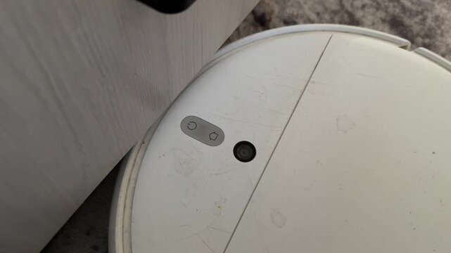 Robot vacuum cleaner trying to pass under cabinet and bumping into furniture corner, smart home cleaning obstacle problem concept