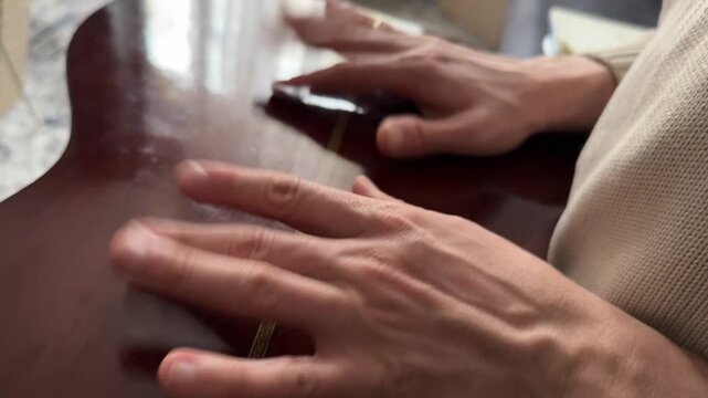 Person tapping fingers on acoustic guitar body close up at home, producing rhythmic percussion sound, improvised music activity, creative hobby concept