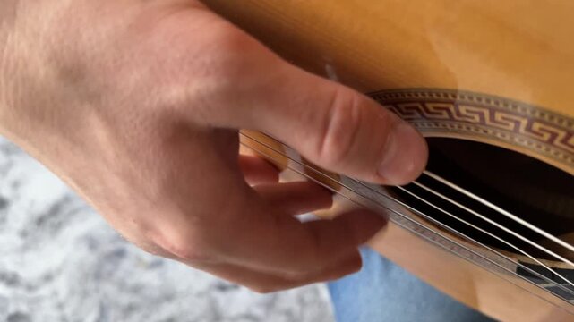 Close-up of a man playing an acoustic guitar. The frame shows the fretboard and the musician's hand
