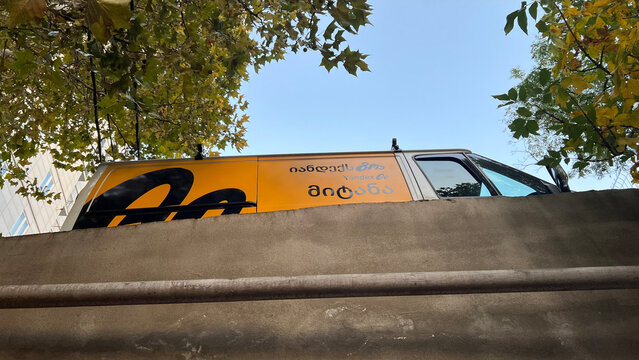 Tbilisi, Georgia - November 22, 2025: Horizontal street city photo. Bottom view. Yellow door with Yandex Go logo on white minivan on parking lot. Concept of shipping, food delivery, traffic jam, taxi