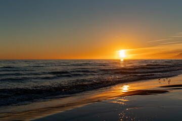 Fototapeta premium Golden sunset over calm sea waves reflecting on the wet sand, creating a peaceful and dreamy seascape with warm light and soft evening atmosphere