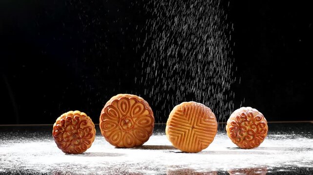 Traditional Chinese mooncakes on a dark reflective surface with white flour falling like snow