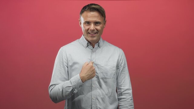 Man handsome with fist to chest facing camera in red studio wearing light button shirt and earnest expression; sincere confidence.