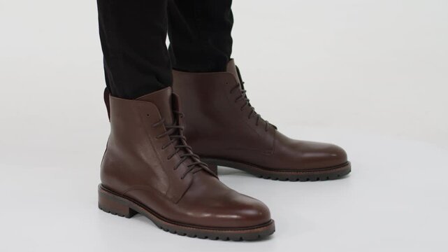 Man wearing brown leather combat boots rotating on a platform isolated on a white background, showcasing footwear fashion