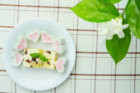 Close-up of marshmallows and a sachima in a white plate, delicious desserts, snacks, decorated with magnolia flower, top view