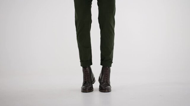 Person in green trousers and brown boots nervously tapping foot on a clean white background, showing impatience or anxiety