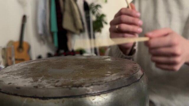 Person hitting metal pot with wooden sticks close up, creating rhythm like drum, improvised percussion activity, creative hobby concept