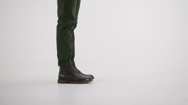 Man in green chinos and brown leather boots walking and stopping, isolated on a white background with copyspace